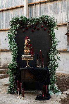 a wedding cake on top of a table with candles and greenery around the edges