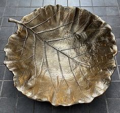 a leaf shaped metal bowl sitting on top of a tile floor