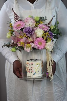 a person holding a cake with flowers in it