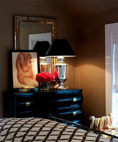 a bedroom with a black dresser and red flowers on it's nightstand next to a window