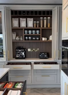 a kitchen with white cabinets and drawers filled with food items, such as coffee machines