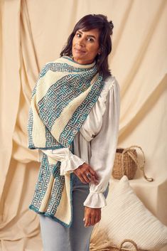 a woman standing in front of a white wall wearing a blue and green shawl