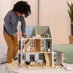 a woman standing in front of a doll house with her hands on the floor and looking at it