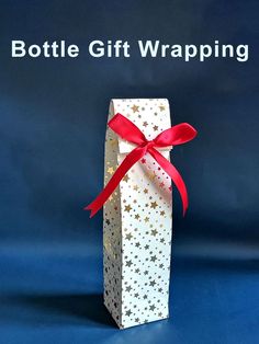 a white paper bag with red ribbon and stars on it, sitting in front of the words bottle gift wrapping