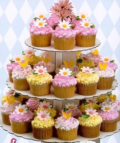 a three tiered cake with cupcakes and flowers on the top is displayed