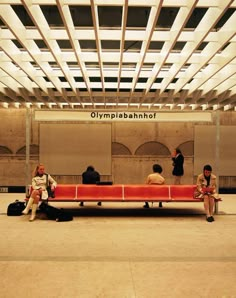 three people sitting on a red bench in an airport