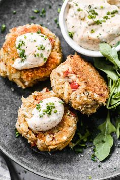 crab cakes with tartar sauce and greens on a black plate, ready to be eaten