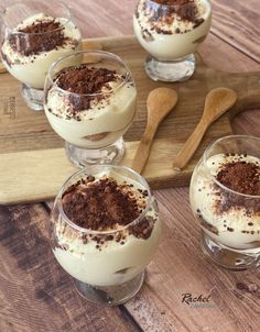 four glasses filled with dessert sitting on top of a wooden table