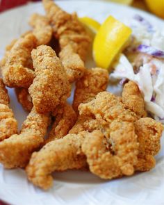 fried food on a plate with lemon wedges and coleslaw