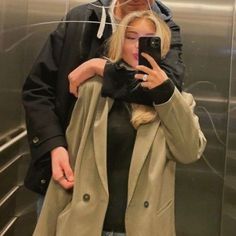 a man and woman standing in front of an elevator taking a selfie with their cell phone