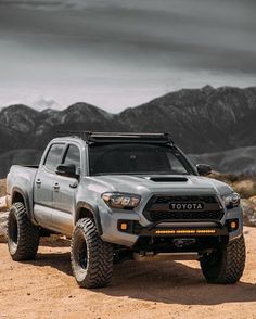 a silver toyota truck parked on top of a dirt field with mountains in the background