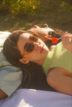 a woman laying on top of a white blanket next to a man with sunglasses and a toothbrush