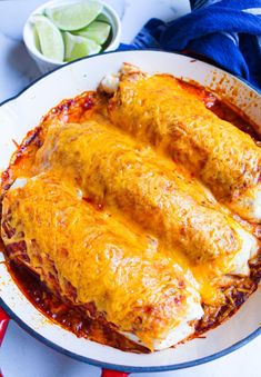 two enchiladas in a white dish with sauce and limes on the side