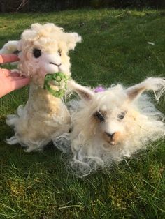 two stuffed animals sitting in the grass with one being petted by someone's hand