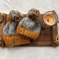 two knitted beanies sitting on top of a wooden tray next to a candle