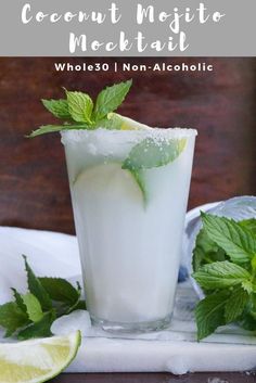 a glass filled with ice and mint sitting on top of a white plate next to limes