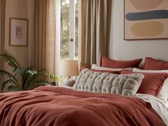 a bed with red sheets and pillows next to a painting on the wall above it