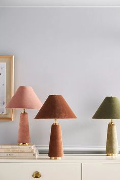 three different colored lamps sitting on top of a white dresser next to a framed photograph