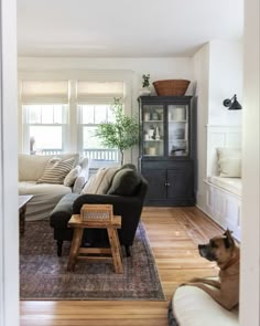 a dog sitting on the floor in front of a living room with white walls and wood floors