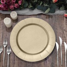 an empty plate with silverware on a wooden table next to pink flowers and candles