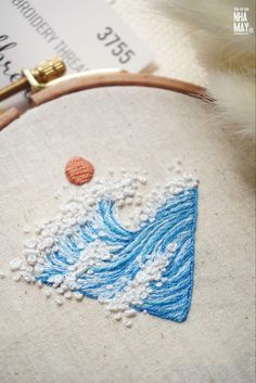 a close up of a cross stitch on a piece of cloth with an embroidered wave