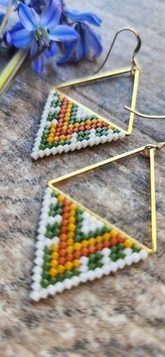 a pair of earrings with beaded triangles on them sitting next to bluebells