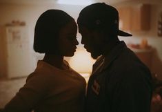 a man and woman standing next to each other in front of a table with a lamp on it