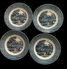 four blue and white plates sitting on top of a black surface with trees in the background