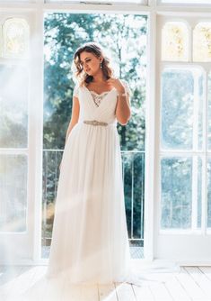 a woman in a white dress standing by a window