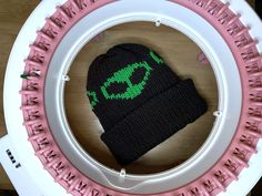 a black and green knitted hat sitting on top of a white plate with pink handles