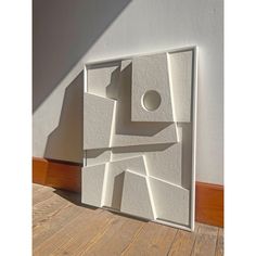 a white sculpture sitting on top of a hard wood floor next to a wall with a shadow