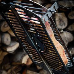 meat is cooking on the grill in front of firewood stacked up and ready to be grilled