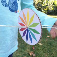 a person holding a colorful paper fan on a string in front of some grass and trees