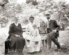 an old black and white photo of a family sitting on a bench in the grass