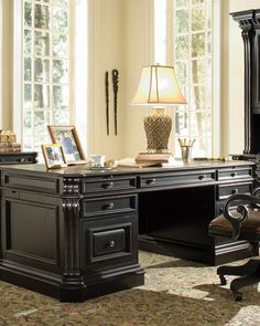 an office desk and chair in front of two windows