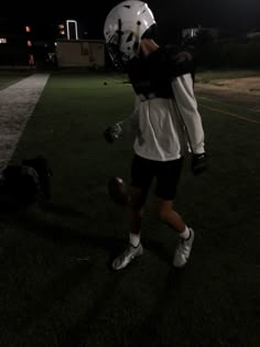 a football player is walking on the field at night with his helmet and glove in hand