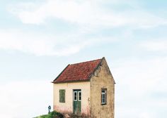 an old house sitting on top of a hill with a red roof and green shutters