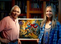 two people standing next to each other in front of bookshelves holding a painting