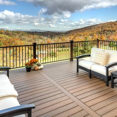 a wooden deck with two chairs and a couch on it, overlooking a valley in the distance