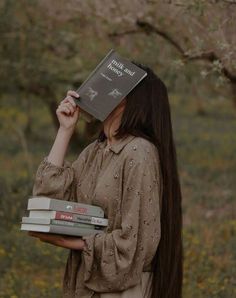 a woman with long hair holding three books in front of her face and looking at the camera