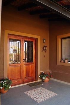 two potted plants sit on the front porch of a home with wooden doors and windows