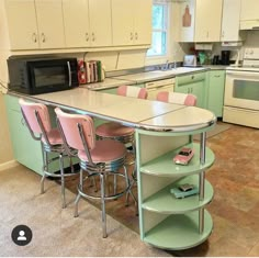 a kitchen with green cabinets and pink chairs in the center, an island that has four stools on it