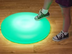 a person standing on top of a green frisbee in the middle of a wooden floor