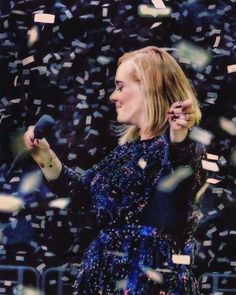 a woman in a blue dress holding a microphone and confetti falling around her