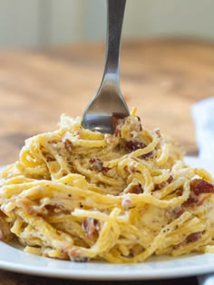 a fork is stuck into some spaghetti on a plate with bacon and parmesan cheese