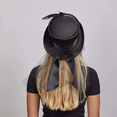 Fancy | Womens Victorian Leather Top Hat combines vintage charm with modern sophistication. Crafted from lightweight USA-made leather, this top hat is adorned with a satin black band and delicate mesh overlay, featuring a bow closure at the back and an antique medallion with feathers. Perfect for making a bold, elegant statement. Material: Lightweight USA Made Leather Shape: Top Hat Trim: Satin Black Band with Mesh Overlay, Bow Back Closure, and Antique Medallion with Feathers Brim Size: 2” Crow Elegant Halloween Fascinator, Elegant Short Brim Halloween Hat, Elegant Top Hat For Halloween Party, Elegant Black Top Hat For Halloween, Victorian Black Top Hat For Party, Black Victorian Top Hat For Party, Elegant Brimmed Hat For Halloween, Elegant Top Hat For Halloween, Elegant Black Hat For Halloween