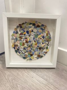 a white frame holding a multicolored glass mosaic in the shape of a circle