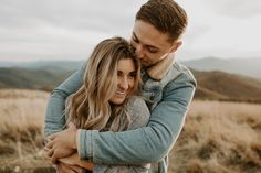 a man and woman hugging each other in the middle of a field with mountains in the background