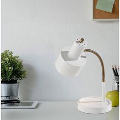 a desk lamp that is on top of a white table next to a potted plant