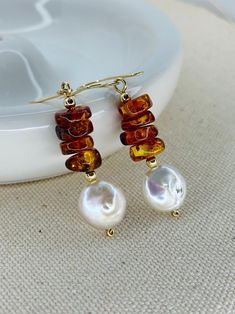 Embody elegance and natural beauty with these beautiful earrings. Handcrafted with Baltic amber gemstones and AAA coin freshwater pearls, these earrings exude sophistication. The 14K gold filled components and accessories complete the luxurious look. Elevate any outfit and feel confident in the unique benefits of our Amber Earrings. 2 1/4 inches length. I design and hand make each piece from my home studio in Port Richey Fl. I take special care in the supply of each component that will be part of the jewelry. I personally select by hand all gemstones and metals to satisfy every desire of my customers, in addition to the quality I offer in my products.  Please allow me 1-3 business days to make and package your piece(s). Your items are expected to be delivered within 7-10 business days afte Cheap Amber Jewelry Gift, Gold Pearl Earrings With Natural Stones, Elegant Baltic Amber Jewelry With Natural Stones, Elegant Orange Pearl Drop Jewelry, Elegant Orange Earrings With Natural Stones, Elegant Baltic Amber Dangle Jewelry, Brown Pearl Drop Earrings As Gift, Brown Pearl Drop Earrings For Gift, Faberge Jewelry